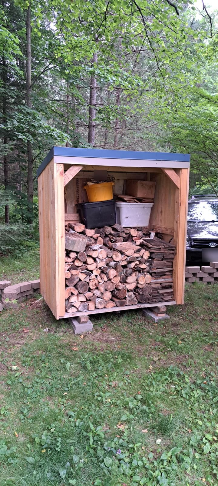 Shed in the woods filled with stacked firewood and storage totes