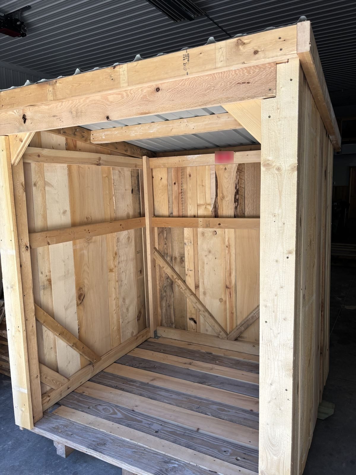 Inside a deep walk-in wood shed showing braced walls and plank floor